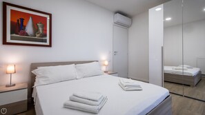 Habitación de hotel moderna con cama, lámparas de noche, un cuadro, unidad de aire acondicionado y un espejo.