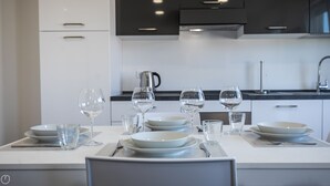 A modern kitchen with white cabinets, a black countertop, and a dining table set for four with wine glasses and plates. - Vat 52 Sub 16 - One Bedroom Apartment, Maximum 5 Guests (Udine)
