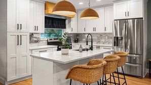 A modern kitchen with white cabinets, stainless steel appliances, a marble backsplash, and a central island with bar stools. - Heated Pool~Pickleball~Hot Tub~Game Room~Basketball~Fire Pit~Bunk Room~4 Kings (Tampa)