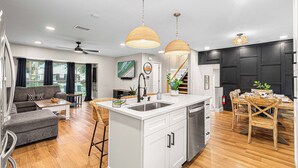 A modern kitchen with a central island, white cabinetry, and a dining area with wooden chairs. - Heated Pool~Pickleball~Hot Tub~Game Room~Basketball~Fire Pit~Bunk Room~4 Kings (Tampa)