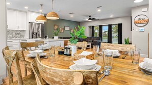 A modern kitchen with white cabinets, a stainless steel refrigerator, and a dining area with wooden chairs and a wooden table set for four. - Heated Pool~Pickleball~Hot Tub~Game Room~Basketball~Fire Pit~Bunk Room~4 Kings (Tampa)