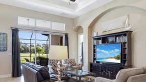 Un salón amplio con televisor grande, asientos cómodos, ventilador de techo y vistas al exterior.