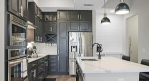 Une cuisine moderne avec des meubles de couleur sombre, des appareils en acier inoxydable et un îlot central.
