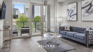 Una sala de estar moderna con una mesa de centro de vidrio, un sofá gris y vistas a la ciudad a través de puertas correderas amplias.
