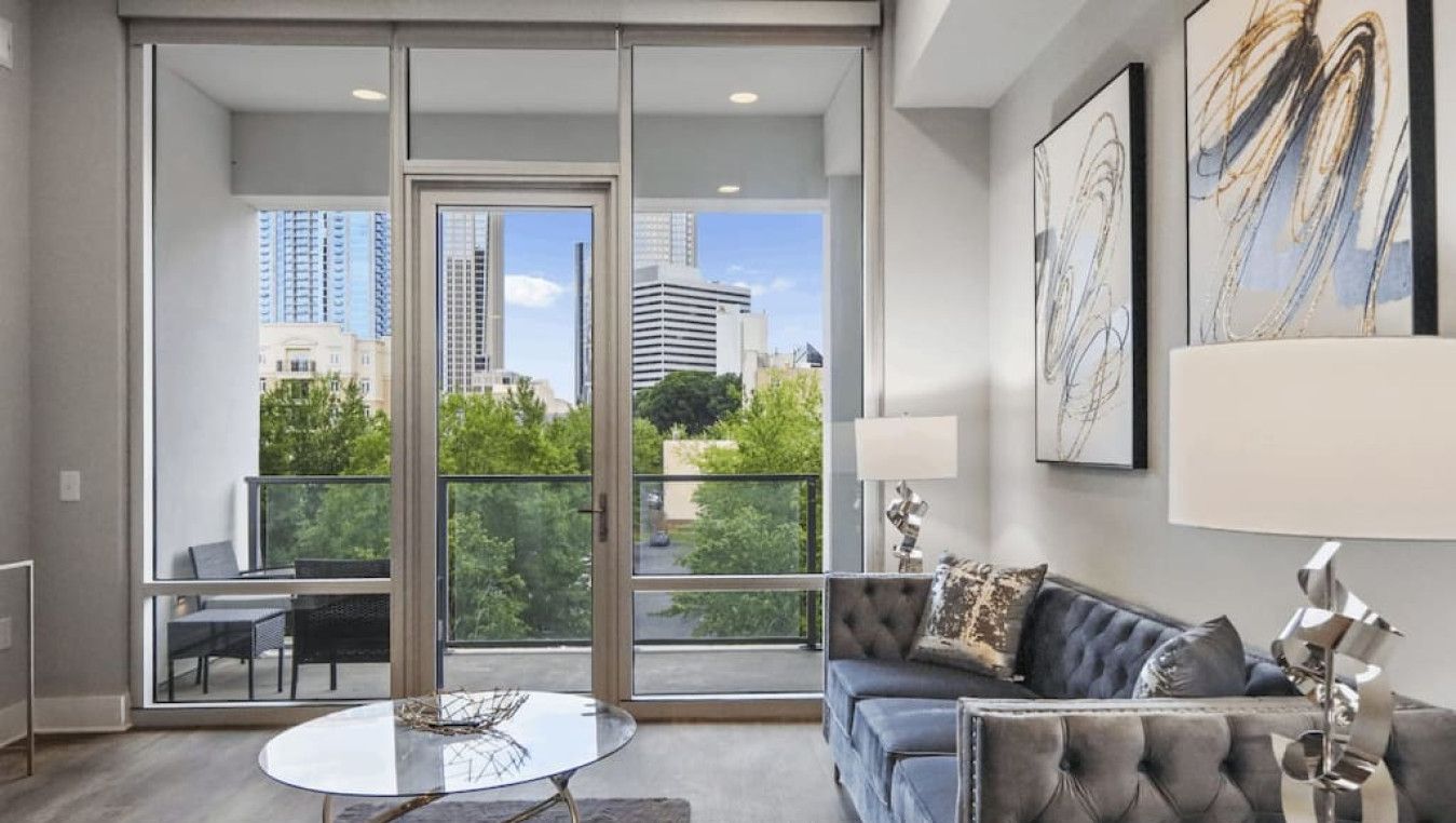 A modern living room with a sofa, a glass coffee table, and a view of the city through large windows.