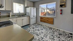 A compact kitchen with white cabinets, a built-in refrigerator, a window with a view, and a fire extinguisher on the wall.