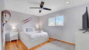 A bedroom with a bed, bedside tables, a ceiling fan, a window, and a TV.