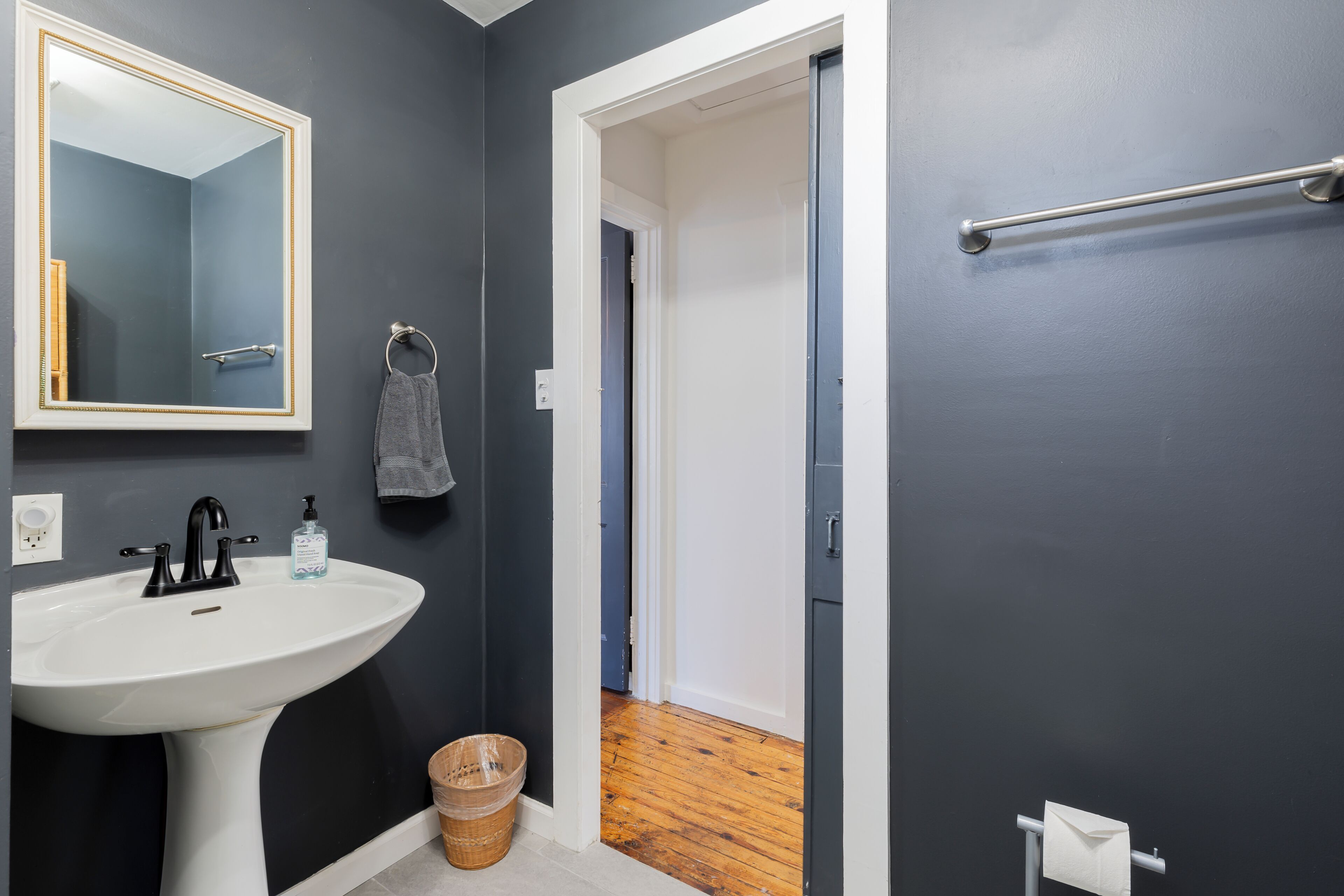 A bathroom with a white sink, a mirror with a gold frame, a towel rack, and a wooden floor.