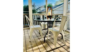 A covered outdoor seating area with a table and chairs, a candle, and a view of a house through large windows. - Cozy Pet-Friendly Beach Cottage 2 Blocks from the Bay (Lower Township)
