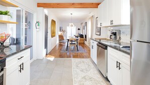 A modern kitchen with white cabinets, a wooden ceiling, and a dining area with a table and chairs. - Cozy Pet-Friendly Beach Cottage 2 Blocks from the Bay (Lower Township)
