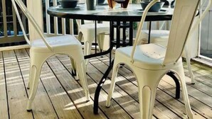 A covered outdoor seating area with a table and chairs, a candle, and a view of a house through large windows. - Cozy Pet-Friendly Beach Cottage 2 Blocks from the Bay (Lower Township)