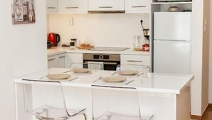 Eine moderne Küche mit weißen Schränken, einer zentralen Kochinsel mit Barhocker, einer Mikrowelle und einem Kühlschrank.