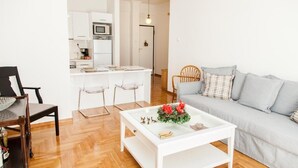 Ein modernes Wohnzimmer mit grauem Sofa, einem weißen Couchtisch mit floraler Dekoration und einem Essbereich mit weißem Tisch und Stühlen.