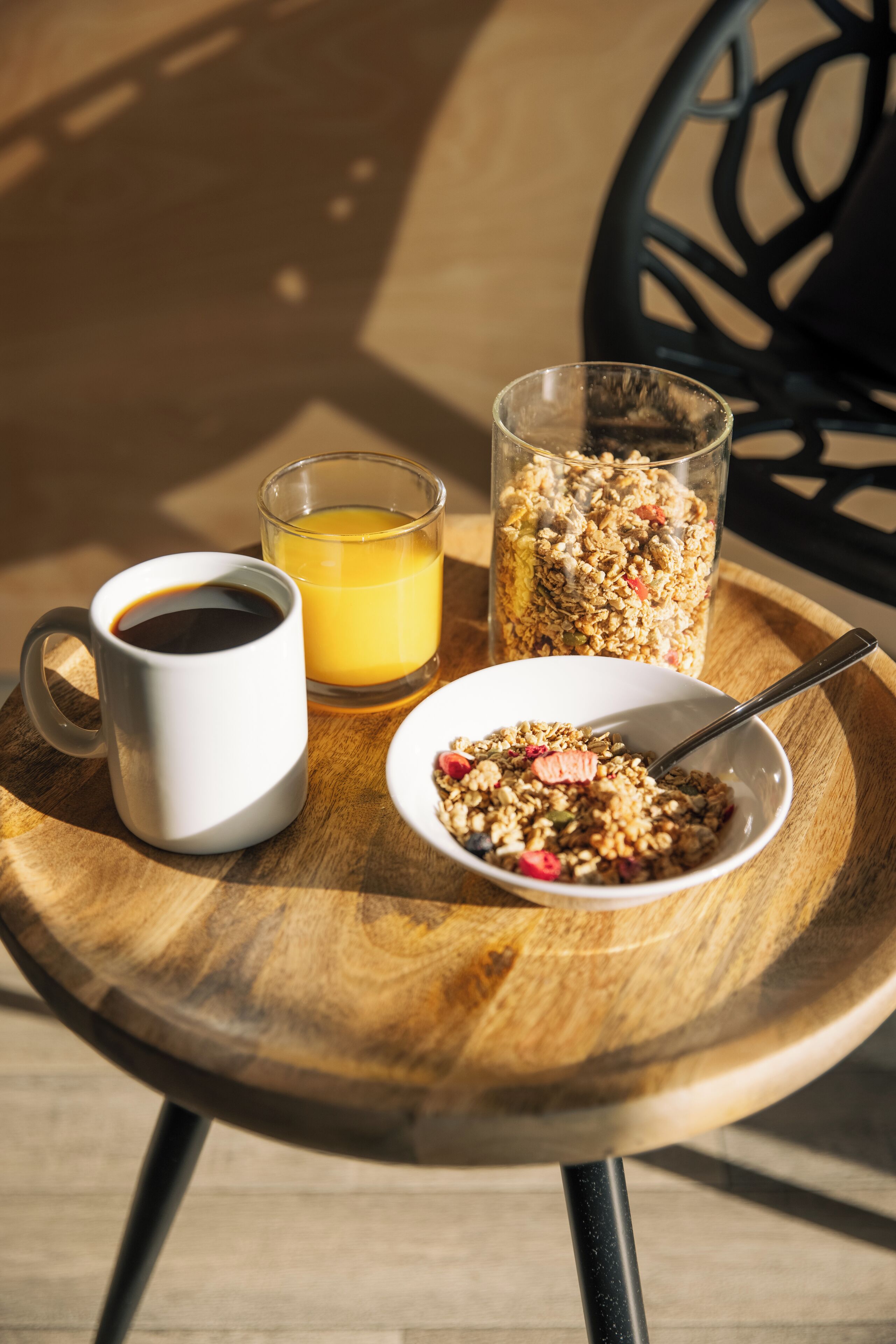 A wooden table with a white mug, a glass of orange juice, a glass of coffee, and a bowl of granola.