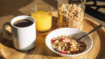A wooden table with a white mug, a glass of orange juice, a glass of coffee, and a bowl of granola.