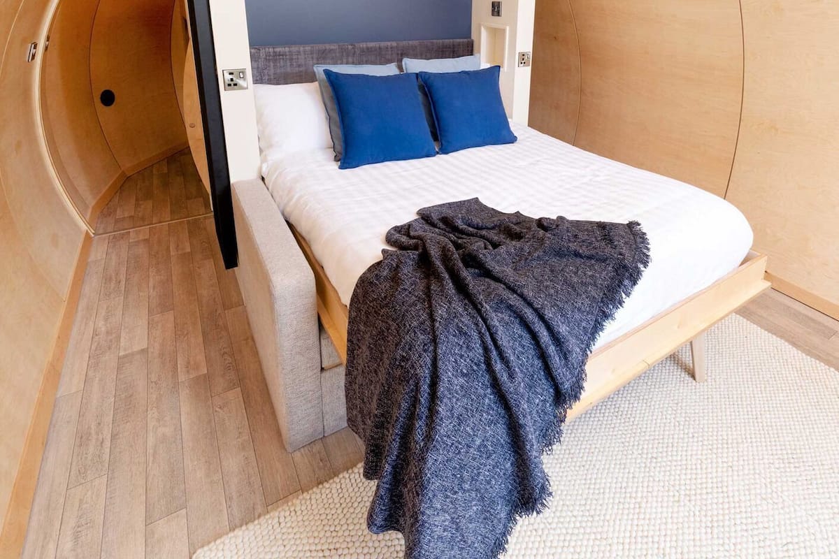 A bedroom with a bed, pillows, a blanket, and a wooden headboard.