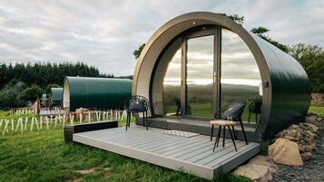 Una estructura abovedada con terraza y zona de estar, rodeada por un paisaje natural.