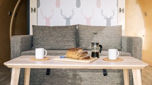 A cozy room with a wooden table, a grey sofa, and a wall with deer silhouettes. - Cardross Estate Glamping (Stirling)