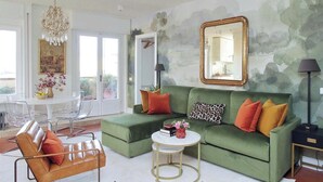 Uma sala de estar com um sofá verde, uma mesa de centro redonda e um candelabro.