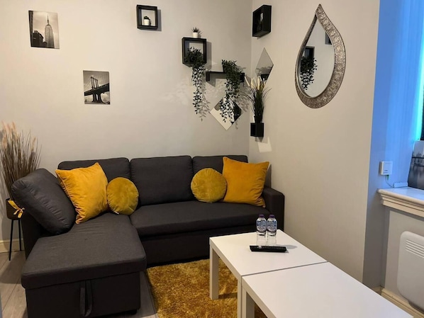 A modern living room with a grey sectional sofa, yellow cushions, a white coffee table, and a large mirror.