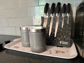 A kitchen counter with a tray holding two containers labeled "Sugar" and "Coffee," and a knife block with knives. - Impeccable 2-bed Apartment by Cardiff City Centre (Cardiff)