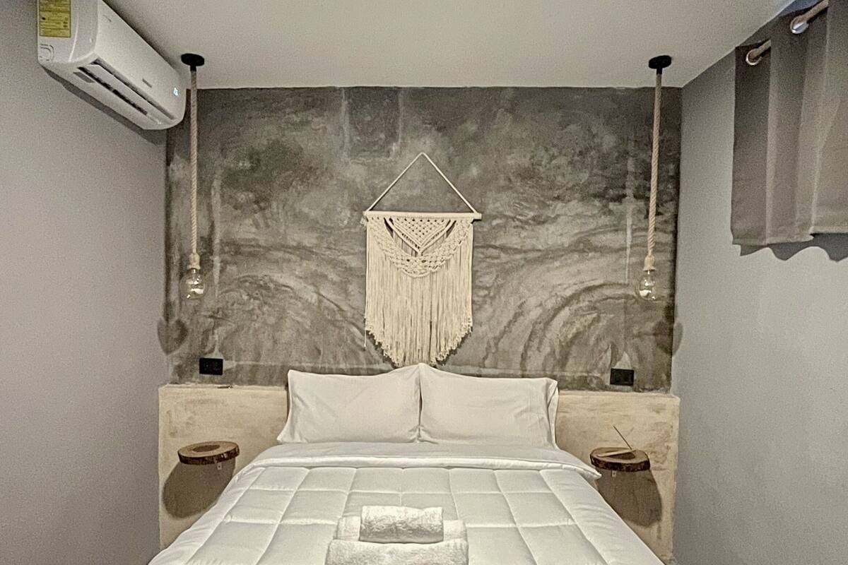 Un dormitorio con cama, un tapiz de macramé y un aire acondicionado de pared.