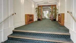 A grand staircase with a patterned carpet, wooden handrails, and potted plants.