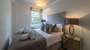 A neatly arranged bedroom with a bed, bedside lamps, a nightstand, and a window with blinds.
