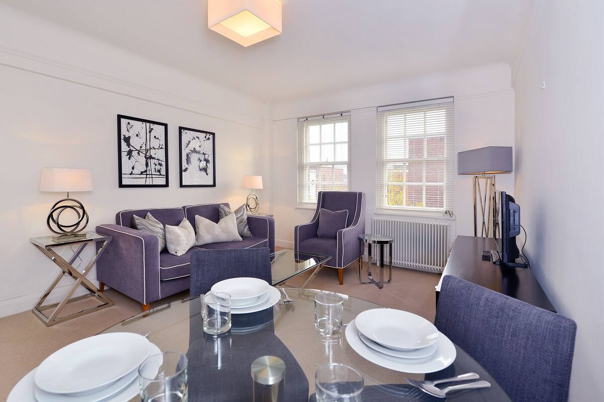 A modern living room with a dining table set for four, a sofa, a chair, and a small side table.