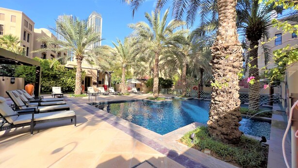 A pool area with lounge chairs and palm trees, surrounded by buildings. - Luxury 2bedroom in Dubai Downtown - Burj Views (Dubai)