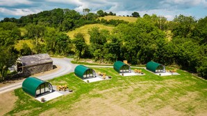 A rural setting with a stone building and four green cylindrical structures with glass walls, each with outdoor seating. - Kinelarty Luxury Glamping Pods (Downpatrick)