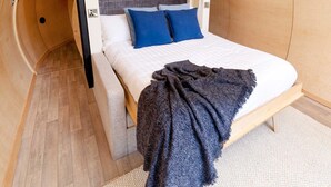 A bedroom with a bed, blue pillows, and a dark blanket. - Kinelarty Luxury Glamping Pods (Downpatrick)