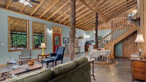 A spacious living area with a high ceiling, wooden beams, a staircase, and a dining area.