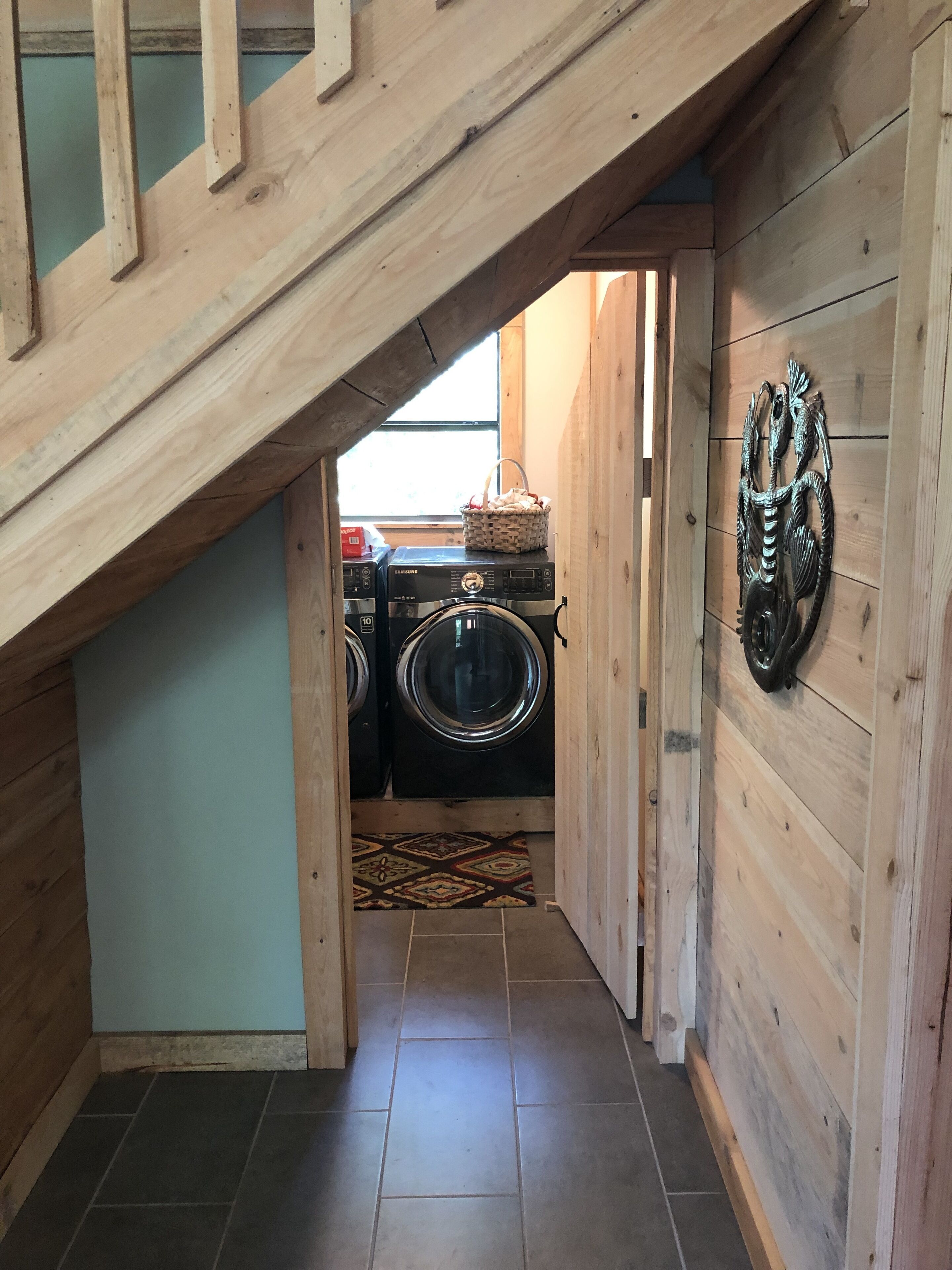 A laundry room with two stacked washers and dryers, a patterned rug, and a decorative wall piece.