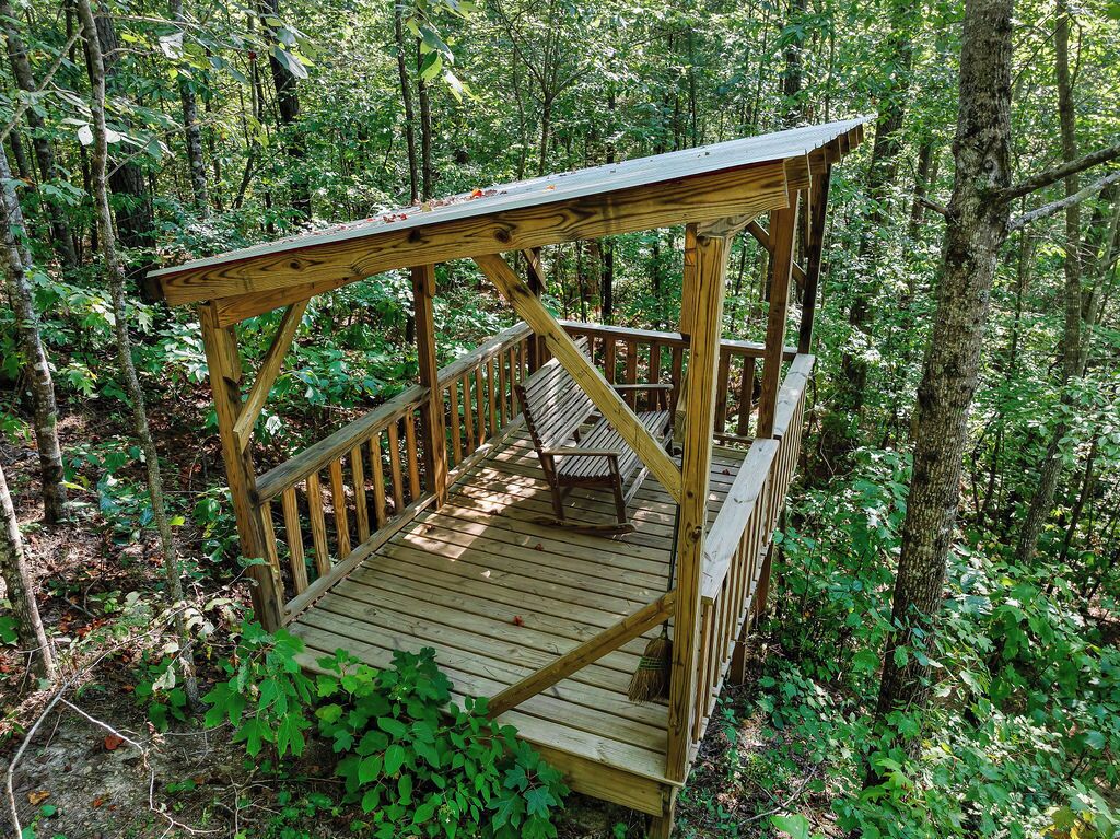 Una terraza de madera con un banco y una mesita pequeña, rodeada de un bosque frondoso.