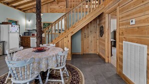 A wooden interior with a dining table, chairs, a staircase, and a kitchen area.