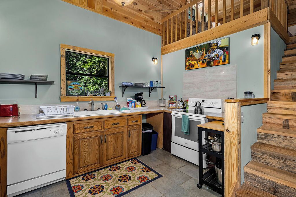 Une cuisine avec des meubles en bois, un lave-vaisselle, une cuisinière et une fenêtre donnant sur un paysage verdoyant.