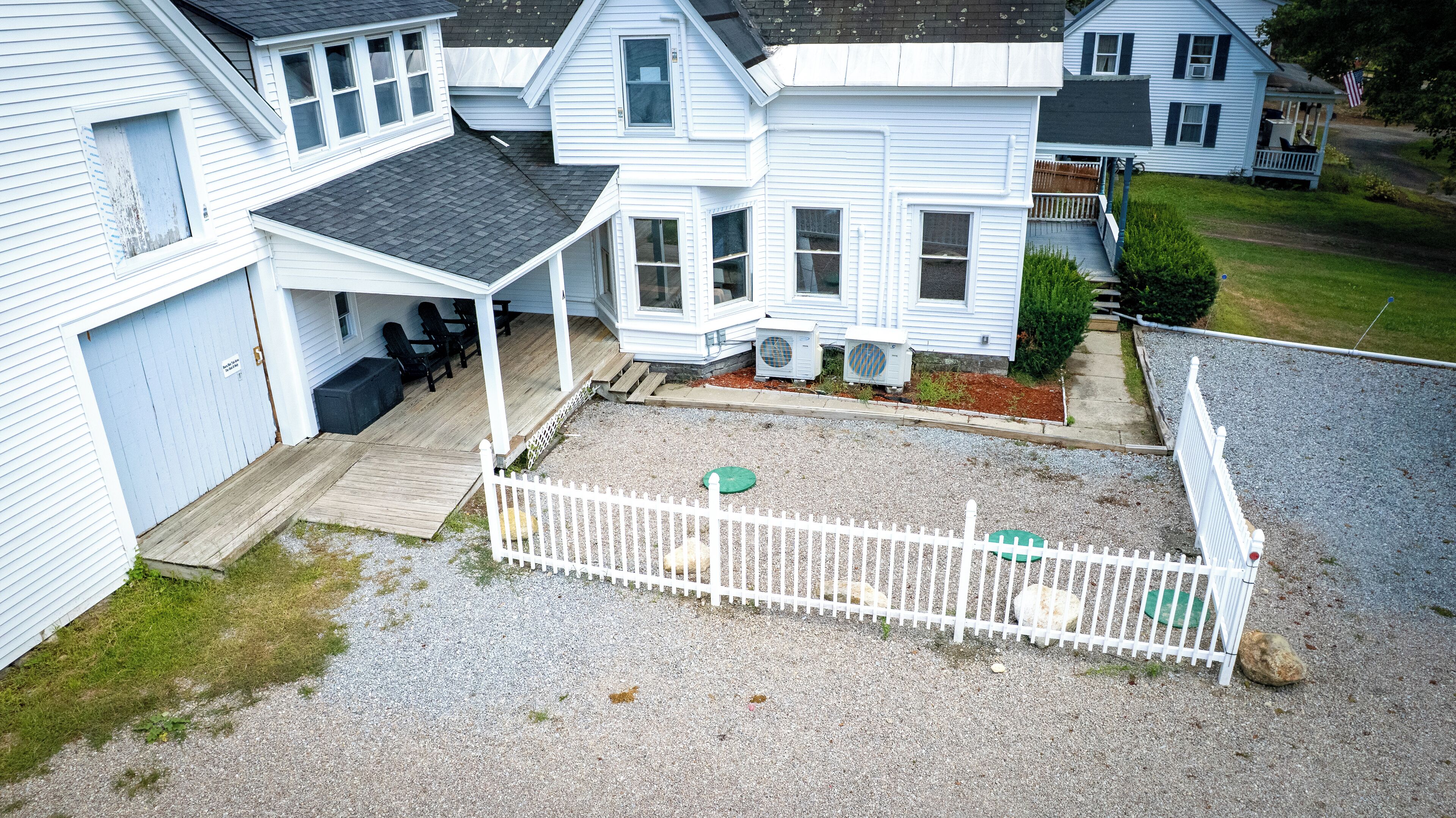 A two-story house with a covered porch, a fenced backyard, and a gravel driveway.