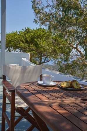 A wooden table with a white cup and a plate of food, set against a backdrop of trees and a clear sky.