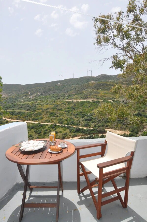 A terrace with a table and a chair, overlooking a hilly landscape with wind turbines.