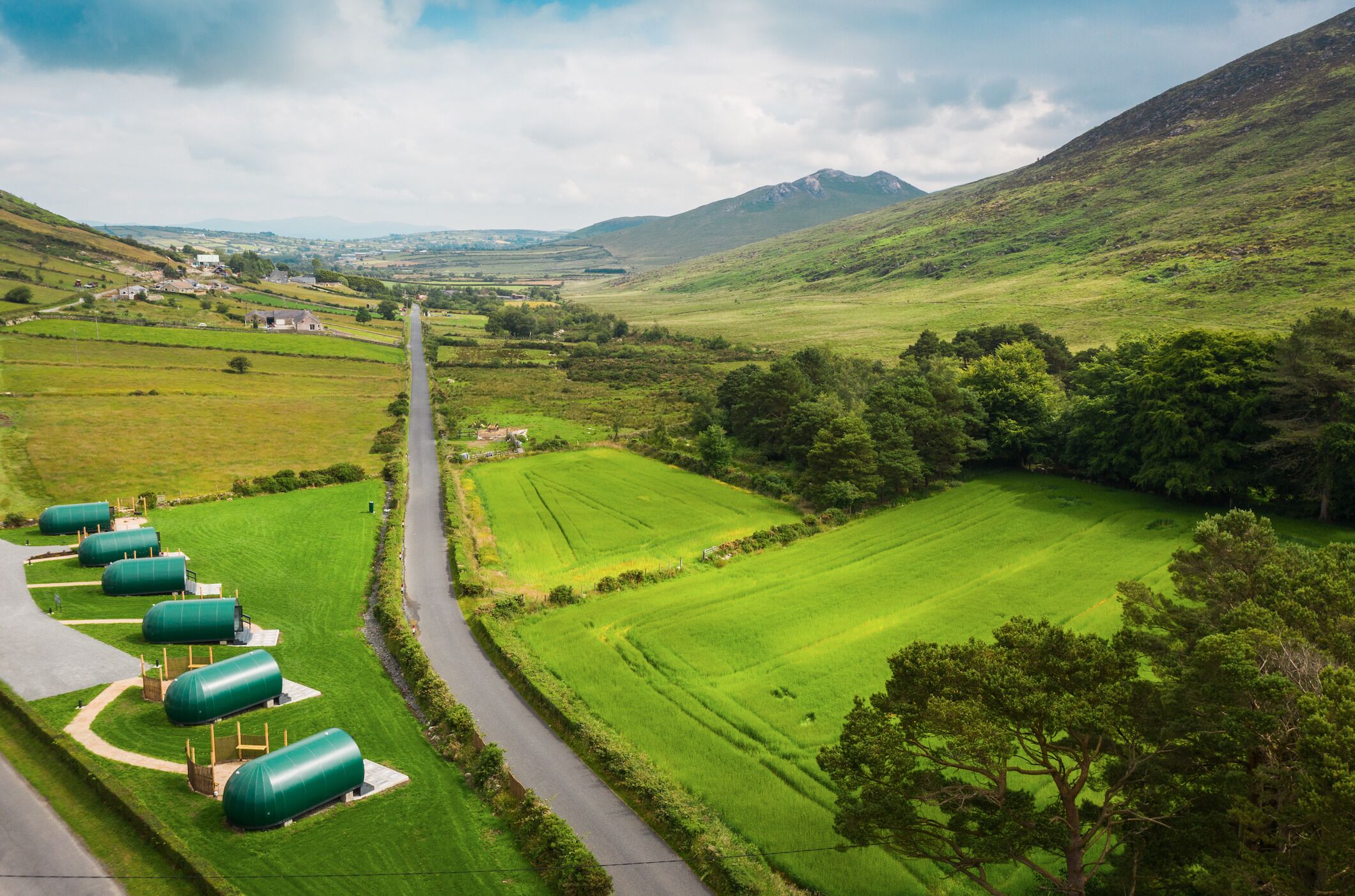 A rural landscape with green fields, a road, and several green cylindrical structures.