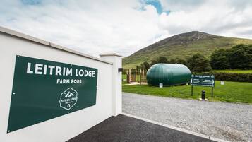A sign for Leitrim Lodge Farm Pods with a view of a hill and a green tank in the background.