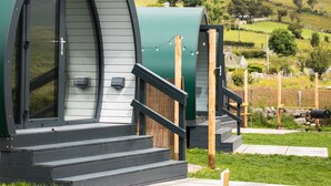 A modern, green, semi-circular building with a glass door, wooden steps, and a grassy area in front. - FURTHER.SPACE at Leitrim Lodge (Newry)