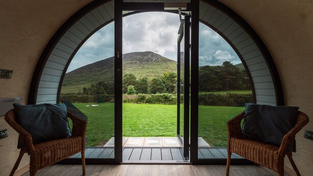 A room with a large arched window offering a view of a green landscape and a hill. There are two wicker chairs with cushions. - FURTHER.SPACE at Leitrim Lodge (Newry)