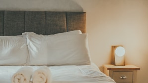 A neatly made bed with white linens and rolled towels, a wooden headboard, and a bedside table with a round mirror. - The Black Isle Apartment (Fortrose)