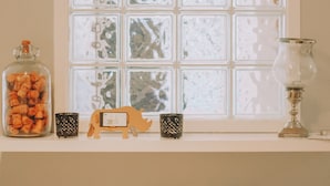 A window with frosted glass panes, a glass jar with corks, a small wooden toy, and two black cups with white speckles on a shelf. - The Black Isle Apartment (Fortrose)