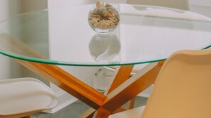 A glass-top table with a bowl of nuts, surrounded by wooden chairs in a bright room with a window. - The Black Isle Apartment (Fortrose)