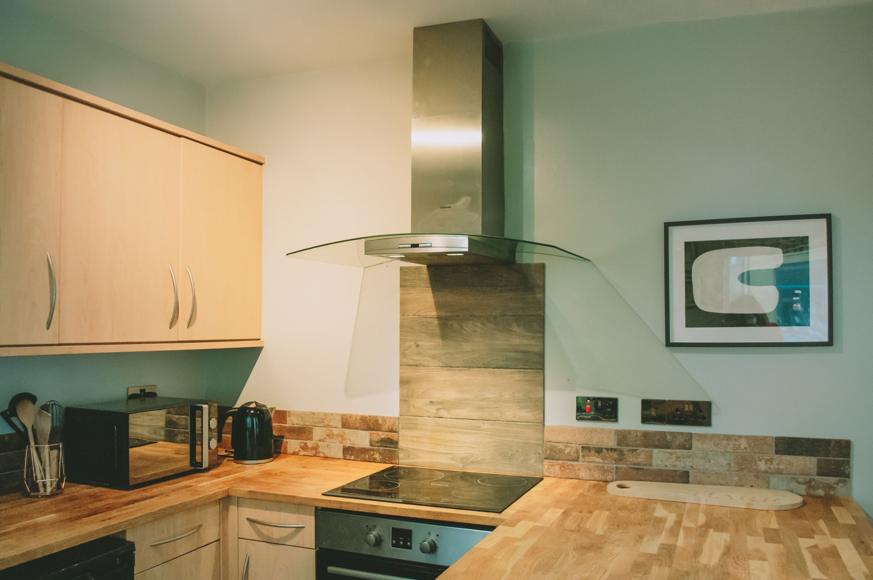 Una cocina moderna con armarios de madera, campana de cristal, estufa integrada y salpicadero con una combinación de azulejos.