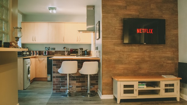 A modern kitchen with wooden cabinets, a built-in oven, and a TV mounted on the wall displaying "NETFLIX". - The Black Isle Apartment (Fortrose)