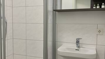 A bathroom with a glass shower enclosure, a white sink with a chrome faucet, and a mirror above the sink.